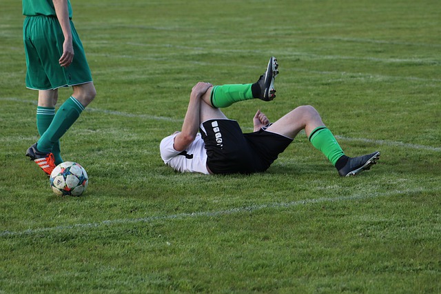 Un futbolista tumbado en el suelo quejándose de su pierna derecha.
