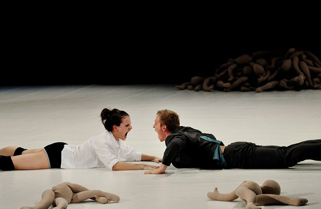 Dos actores tumbados en el suelo se gritan.