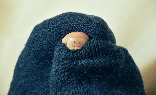 Un calcetín con agujero del que asoma el dedo gordo con una sonrisa pintada en la uña. 