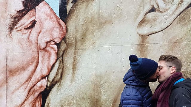 Una pareja se besa junto al muro de Berlín