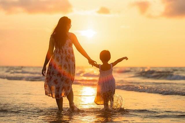 Una madre y su hija pasean juntas por la playa con una luz algo oscura. 