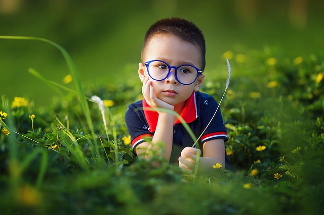 Fotografía de un niño tumbado sobre la hierba. La característica más principal de este niño son unas gafas redondas con aspecto de inteligencia