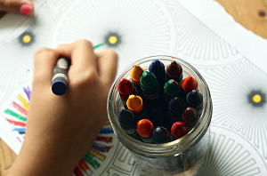 Una mano dibujando con un bote de lápices de colores