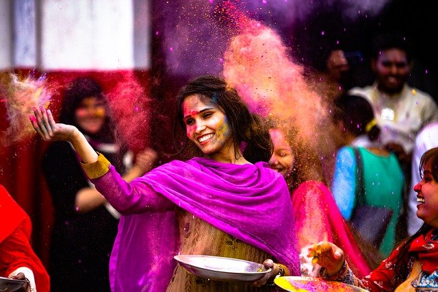 Una mujer de la India viste un sari de colores alegres y espolvora pigmentos por el aire.