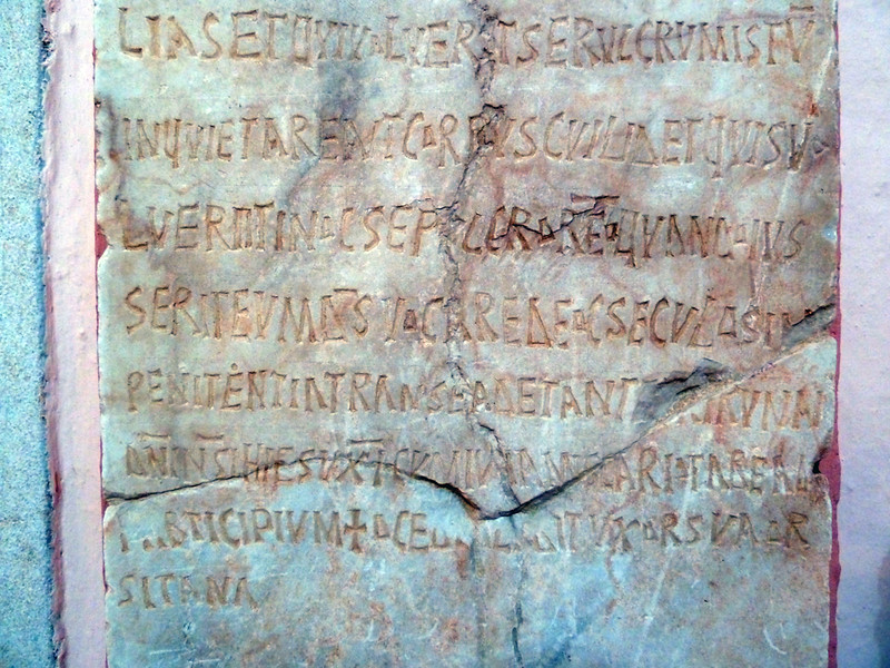 Inscripción latina grabada en piedra con roturas y desgaste