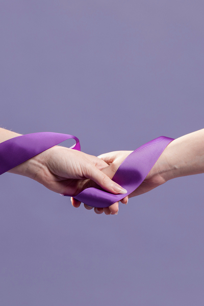 Manos de mujer entrelazadas por una cinta violeta.