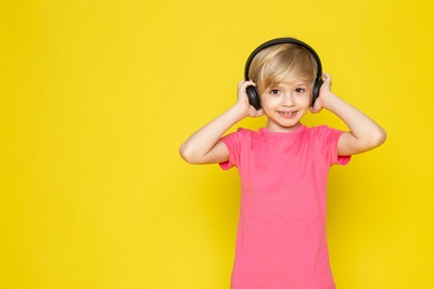 Niño con camiseta rosa y auriculares negros escuchando música.